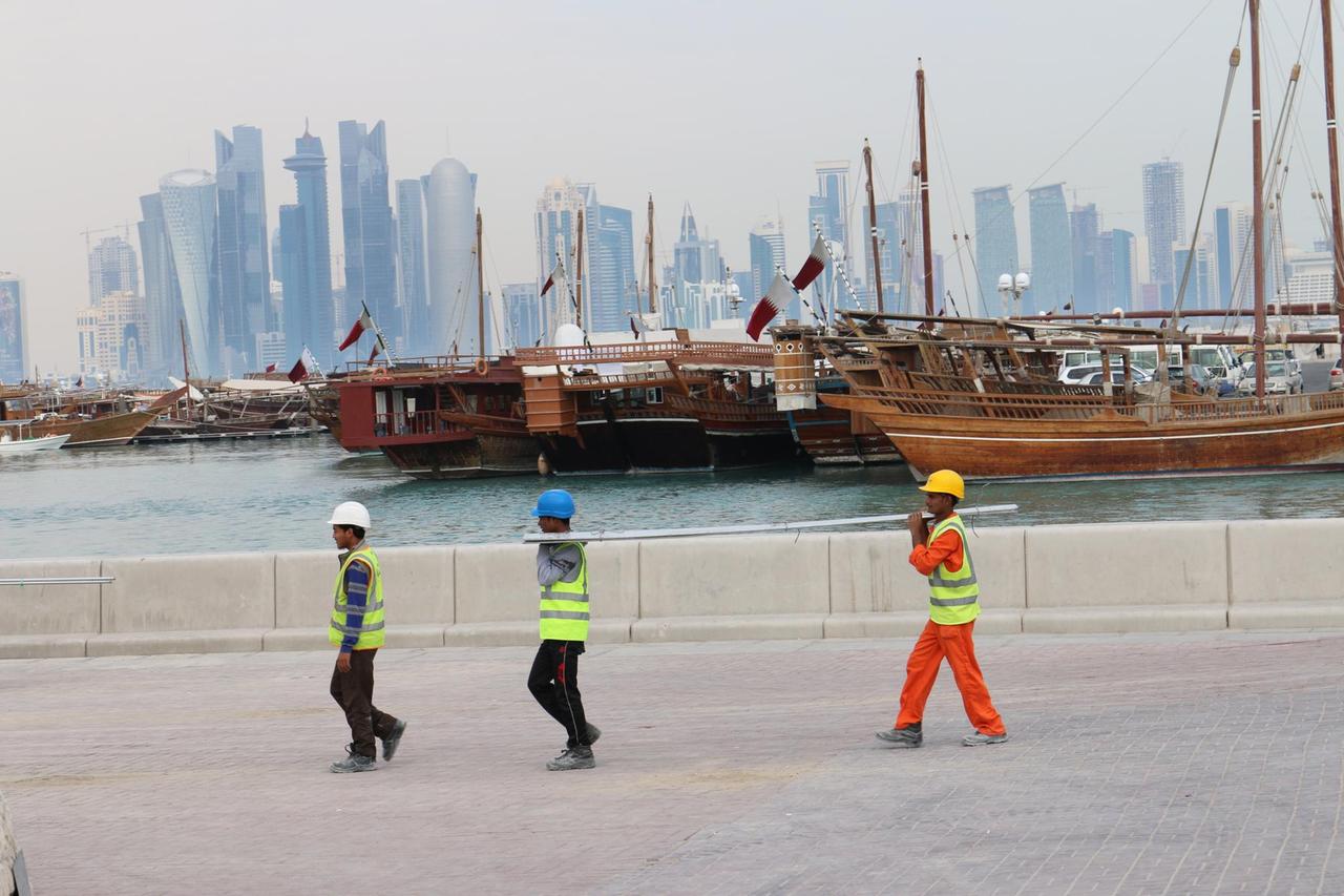 Drei Bauarbeiter gehen am Dau-Hafen entlang mit der Skyline der katarischen Hauptstadt Doha im Hintergrund. Drei Bauarbeiter gehen am Dau-Hafen entlang mit der Skyline der katarischen Hauptstadt Doha im Hintergrund.