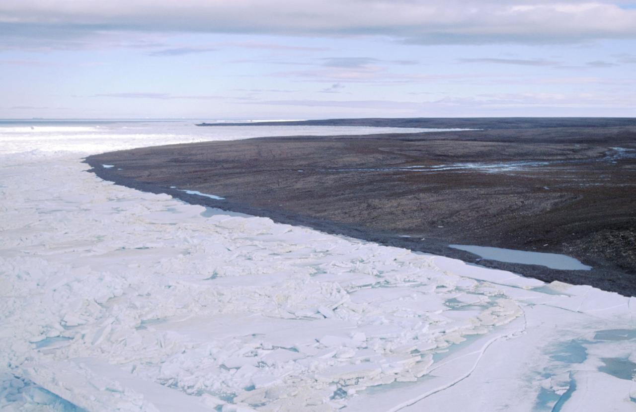 Blick über eine durch Dauerfrost (Permafrost) gezeichnete Landschaft auf der zur Russland gehörenden Bolschewik Insel, während im Vordergrund noch Packeis herrscht ist im Hintergrund die Landschaft schon aufgetaut und schlammig.  