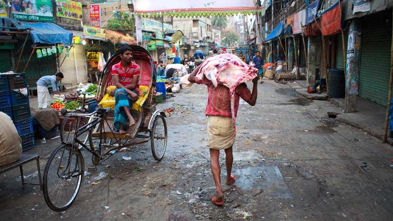 Ein Lieferant trägt ein großes Stück Fleisch über einen Gemüsemarkt in Bangladesch.
