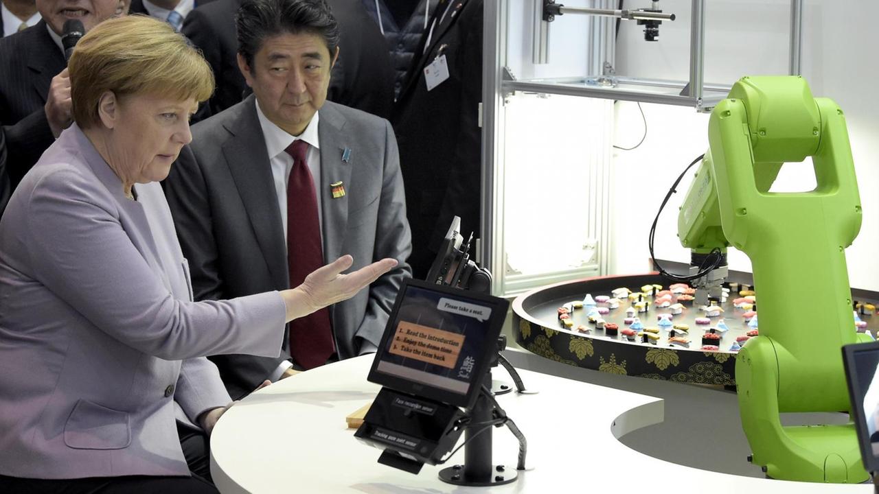 Bundeskanzlerin Angela Merkel und Japans Premier Shinzo Abe sitzen an einem Tisch, vor ihnen ein Tabletcomputer zur Steuerung eines grünen Roboterarms. Bundeskanzlerin Angela Merkel und Japans Premier Shinzo Abe sitzen an einem Tisch, vor ihnen ein Tabletcomputer zur Steuerung eines grünen Roboterarms.