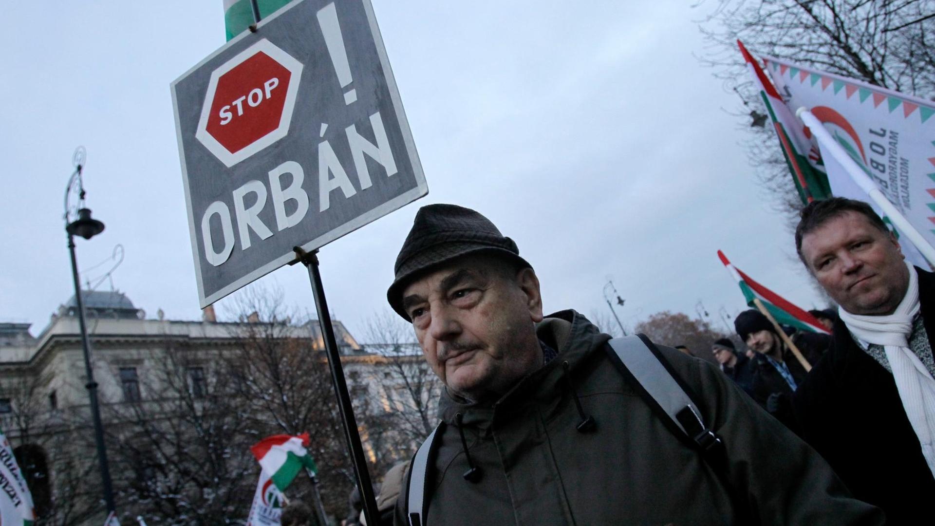 Ein Mann hält auf einer Demonstration in Budapest ein Schild mit der Aufschrift "Stop Orban". Ein Mann hält auf einer Demonstration in Budapest ein Schild mit der Aufschrift "Stop Orban".