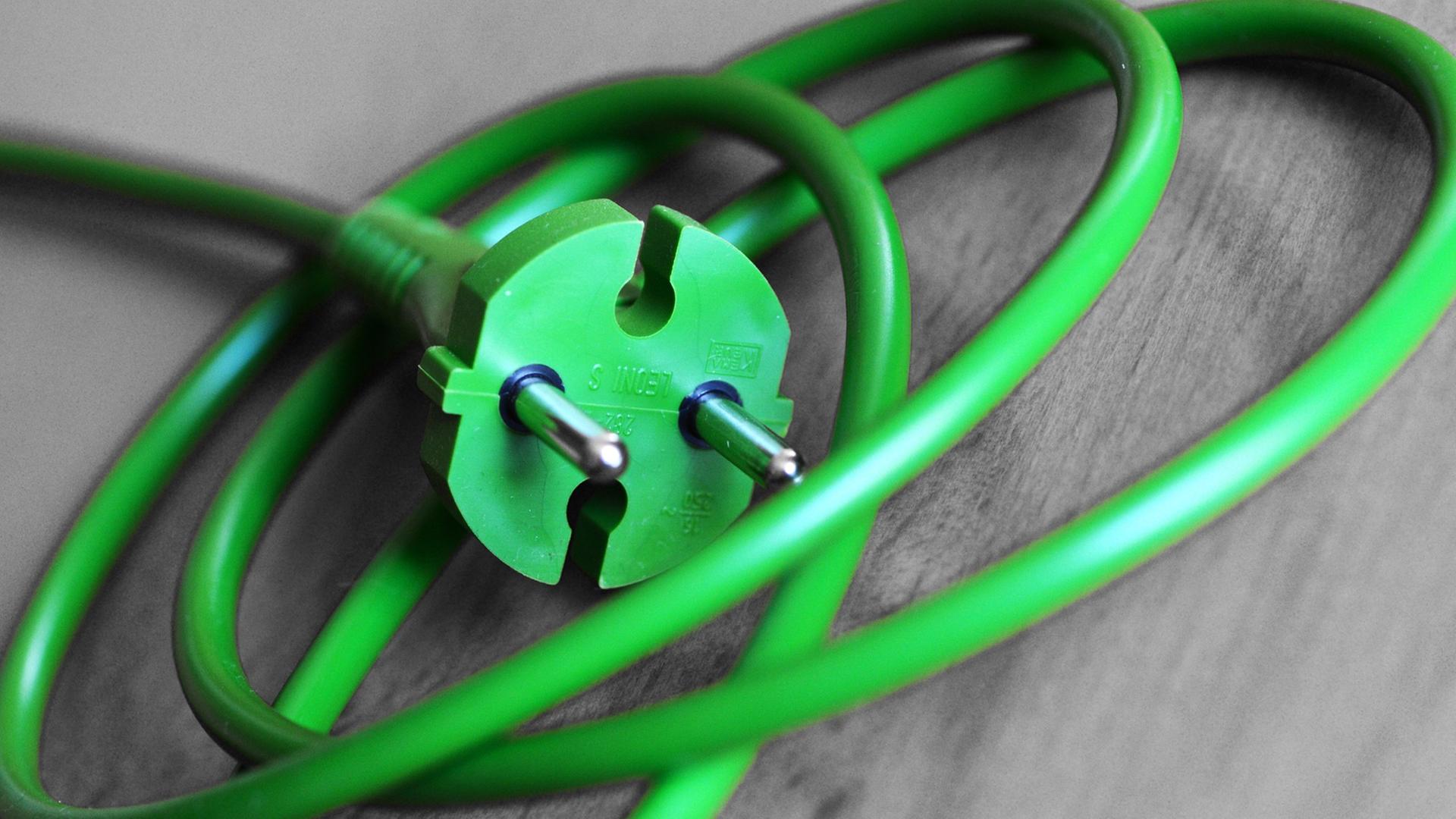 Ein grünes Stromkabel mit einem grünen Stromstecker liegt auf dem Boden. Ein grünes Stromkabel mit einem grünen Stromstecker liegt auf dem Boden.