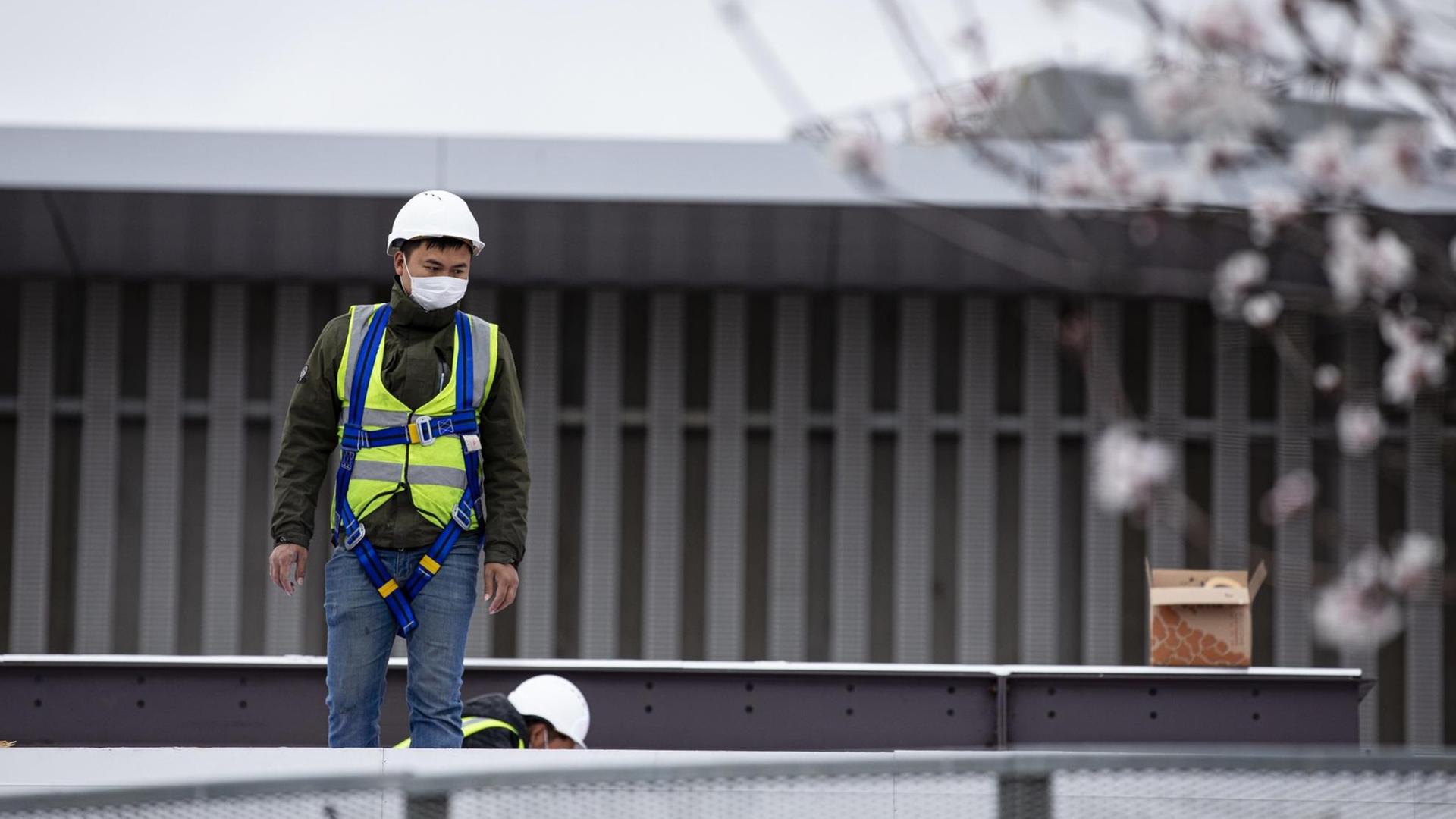 Ein Arbeiter steht mit einem Mundschutz auf einem Dach. Vorbereitungen zum Mobile World Congress in Barcelona 2020 Ein Arbeiter steht mit einem Mundschutz auf einem Dach. Vorbereitungen zum Mobile World Congress in Barcelona 2020