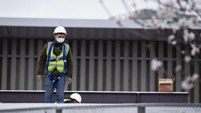 Ein Arbeiter steht mit einem Mundschutz auf einem Dach. Vorbereitungen zum Mobile World Congress in Barcelona 2020