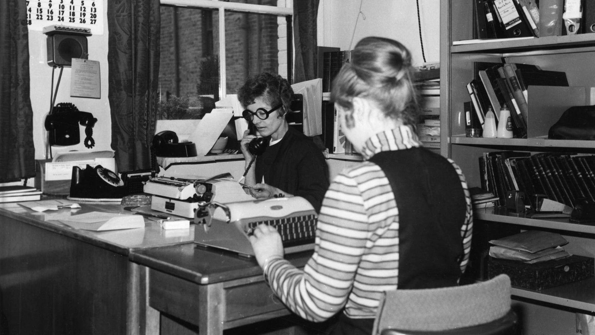 Archivbild: zwei Frauen sitzen in einem Büro, eine telefoniert, die andere tippt auf einer Schreibmaschine