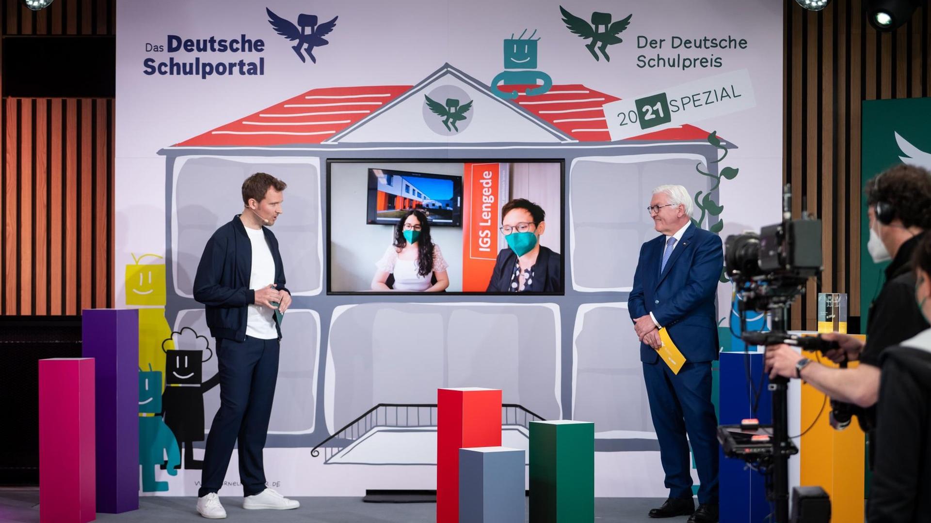 Auf dem Bild ist der Bundes-Präsident zu sehen, als er den Schul-Preis verleiht. Auch der Moderator Lennert Brinkhoff ist auf der Bühne. Auf dem Bild ist der Bundes-Präsident zu sehen, als er den Schul-Preis verleiht. Auch der Moderator Lennert Brinkhoff ist auf der Bühne.
