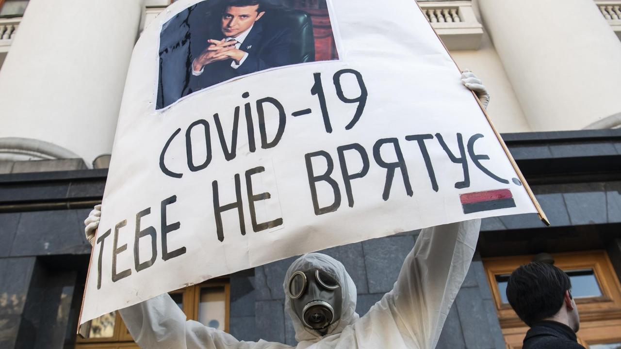 Ein urkainischer Verteran mit einer Gesichtsmaske hält ein Schild in die Luft. Darauf steht "COVID-19 wird Dich nicht retten". Die Botschaft ist an den urkainischen Präsidenten Wolodymyr Selensky gerichtet