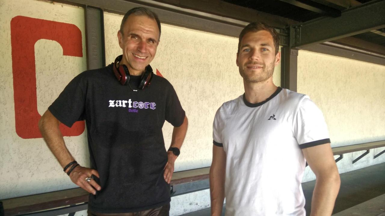 Zwei Männer, der eine im besten Alter, der andere etwas jünger, stehen in einem Fußballstadion und lachen freundlich in die Kamera. Zwei Männer, der eine im besten Alter, der andere etwas jünger, stehen in einem Fußballstadion und lachen freundlich in die Kamera.