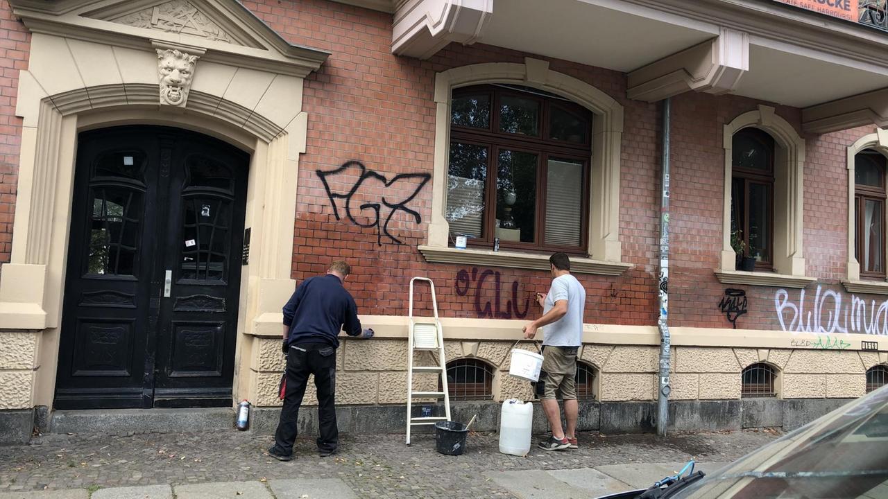 Zwei Arbeiter stehen vor einer Hauswand und übermalen Graffitis.