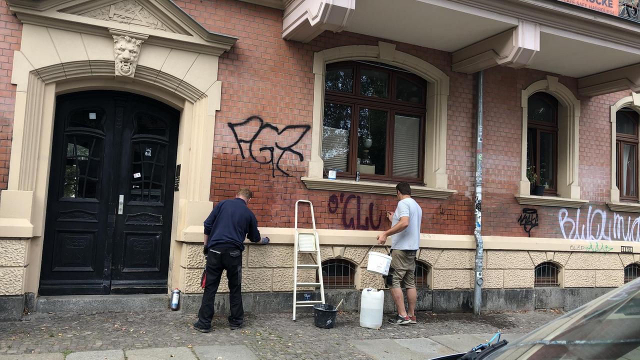 Zwei Arbeiter stehen vor einer Hauswand und übermalen Graffitis. Zwei Arbeiter stehen vor einer Hauswand und übermalen Graffitis.
