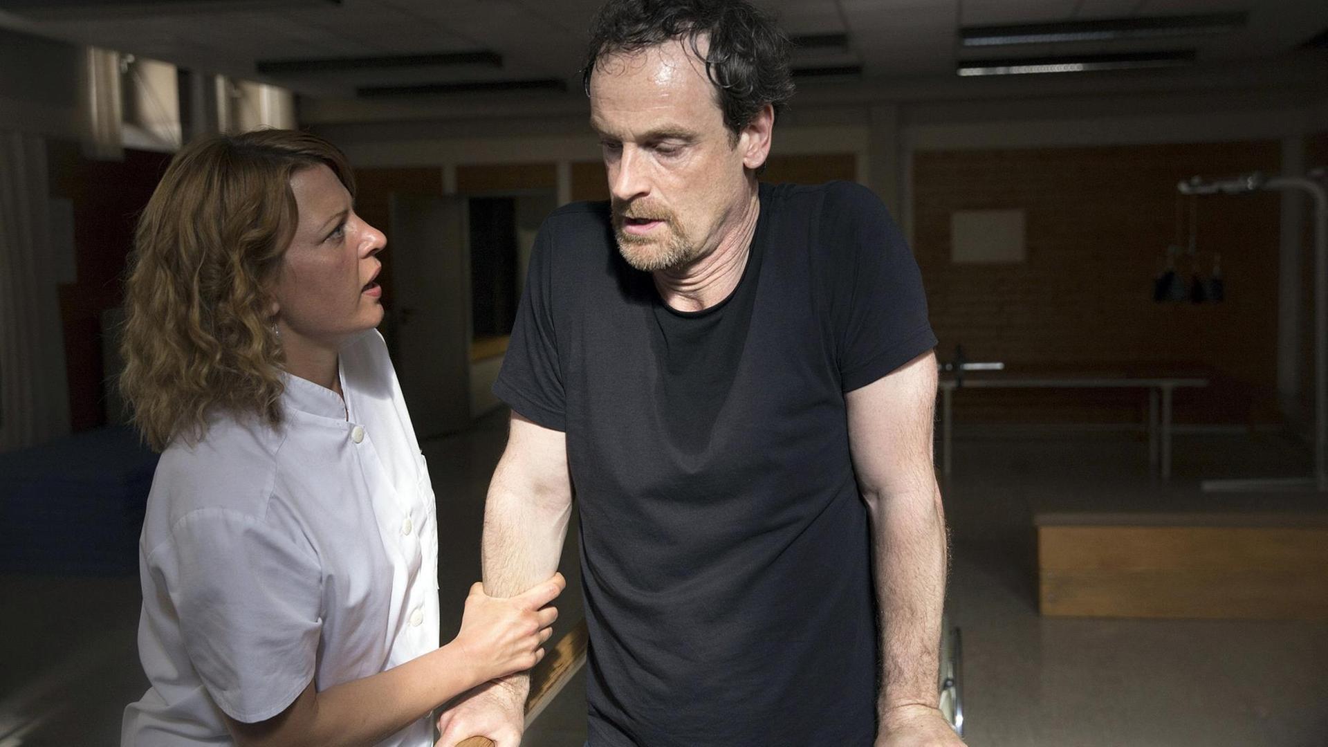 Szene aus der 4. Staffel der Serie "Weissensee": Petra Zeiler (Jördis Triebel) ist beeindruckt vom Kampfgeist ihres Patienten Falk (Jörg Hartmann). Beide stehen an einem Barren. Szene aus der 4. Staffel der Serie "Weissensee": Petra Zeiler (Jördis Triebel) ist beeindruckt vom Kampfgeist ihres Patienten Falk (Jörg Hartmann). Beide stehen an einem Barren.