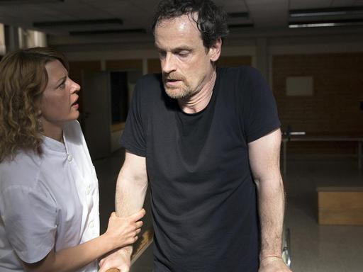 Szene aus der 4. Staffel der Serie "Weissensee": Petra Zeiler (Jördis Triebel) ist beeindruckt vom Kampfgeist ihres Patienten Falk (Jörg Hartmann). Beide stehen an einem Barren.