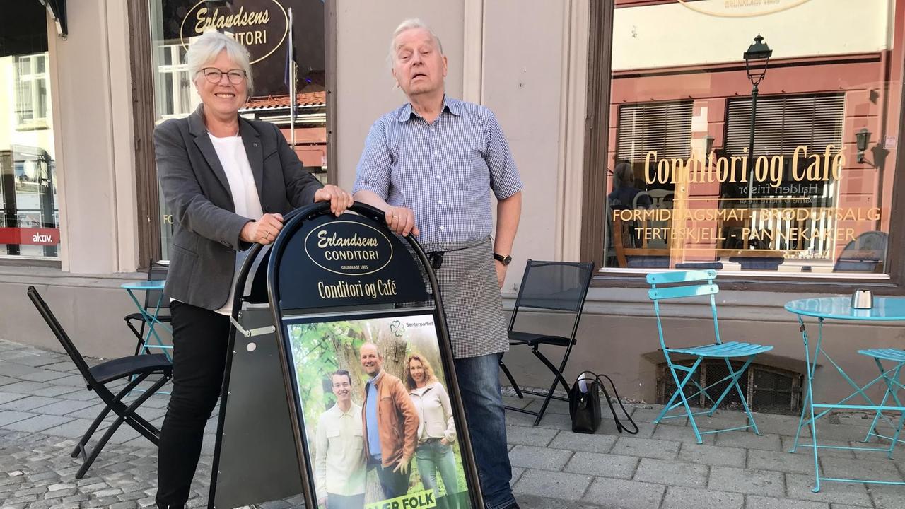 Mann und Frau stehen vor einem Kaffee in der Fußgängerzone. Sie lehnen sich an an eine Werbetafel. Mann und Frau stehen vor einem Kaffee in der Fußgängerzone. Sie lehnen sich an an eine Werbetafel.