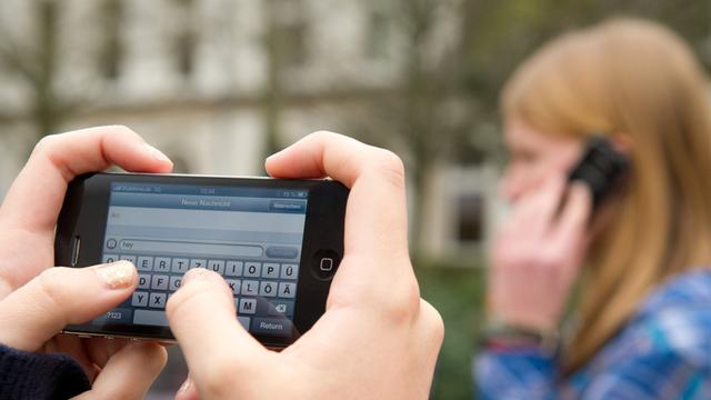Schüler schreiben SMS und telefonieren auf einem Schulhof 