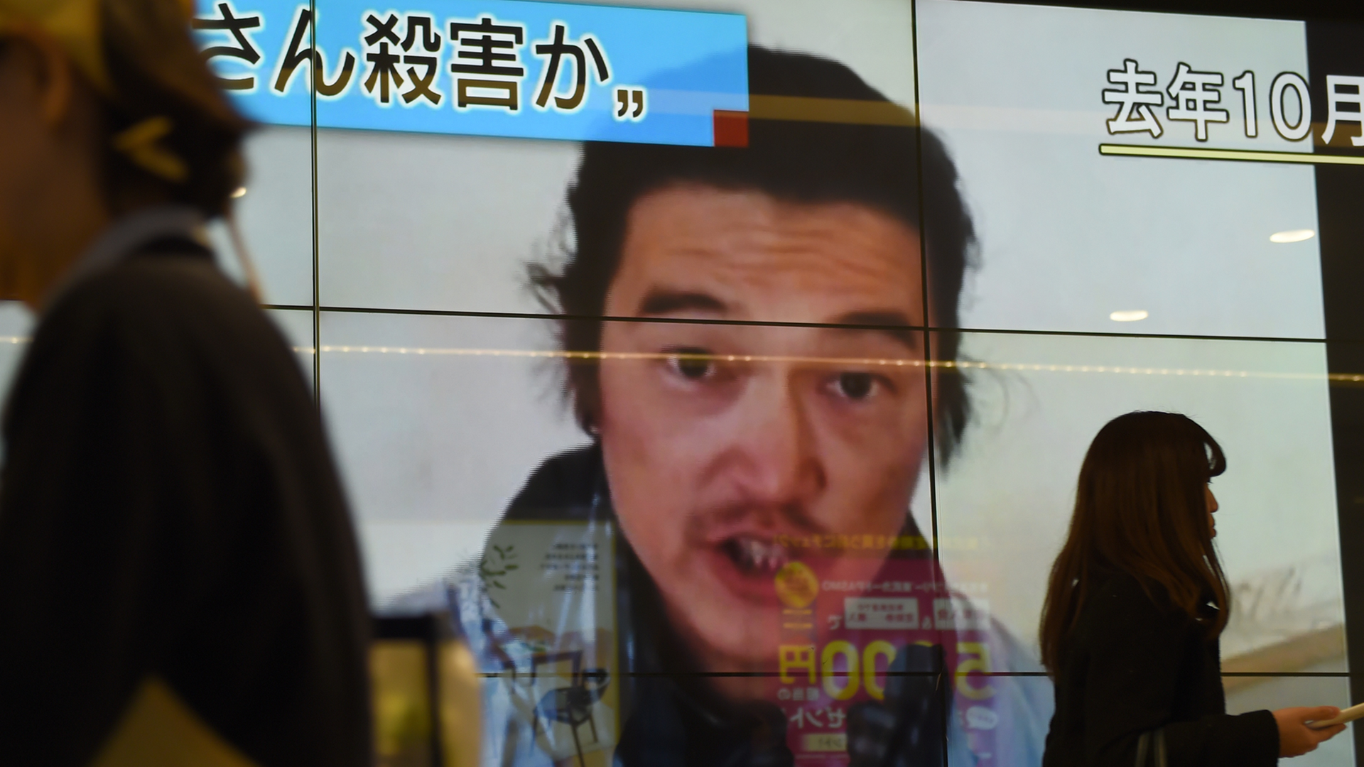 Passanten laufen an einer Leinwand vorbei. Zu sehen ist der Bericht über die Ermordung des japanischen Journalisten Kenji Goto. Passanten laufen an einer Leinwand vorbei. Zu sehen ist der Bericht über die Ermordung des japanischen Journalisten Kenji Goto.