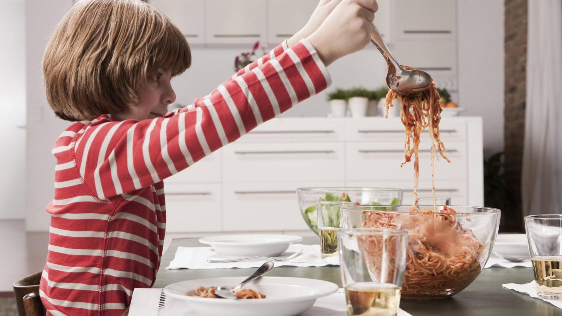 Ein Junge füllt sich Spaghetti mit Tomatensoße aus einer Schüssel auf seinen Teller Ein Junge füllt sich Spaghetti mit Tomatensoße aus einer Schüssel auf seinen Teller