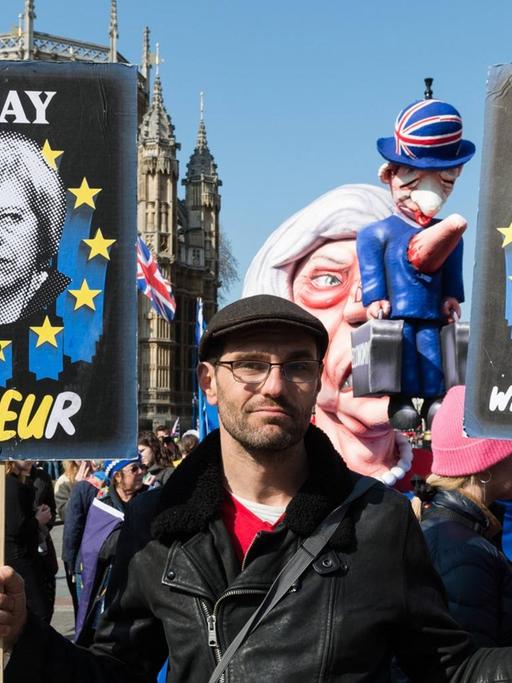 Ein Anti-Brexit-Demonstrant hält Plakate von May und Corbyn in den Händen