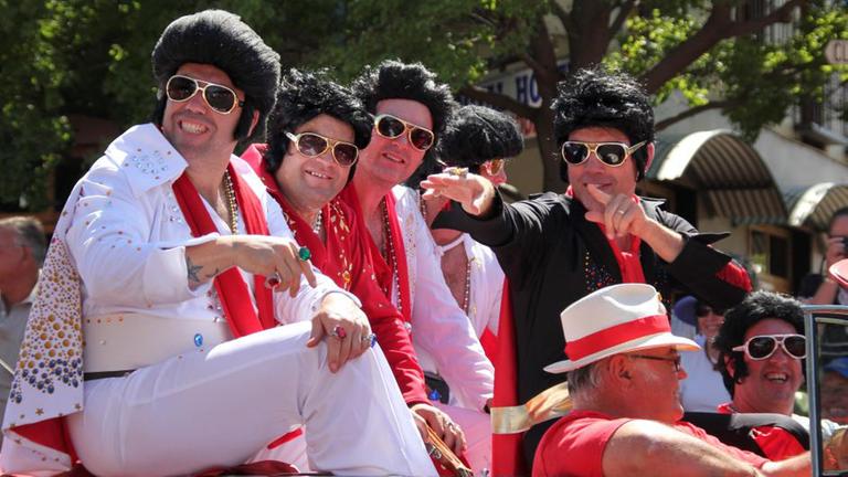 Vier als Elvis verkleidete Männer fahren in einem Auto durch Parkes. Vier als Elvis verkleidete Männer fahren in einem Auto durch Parkes.