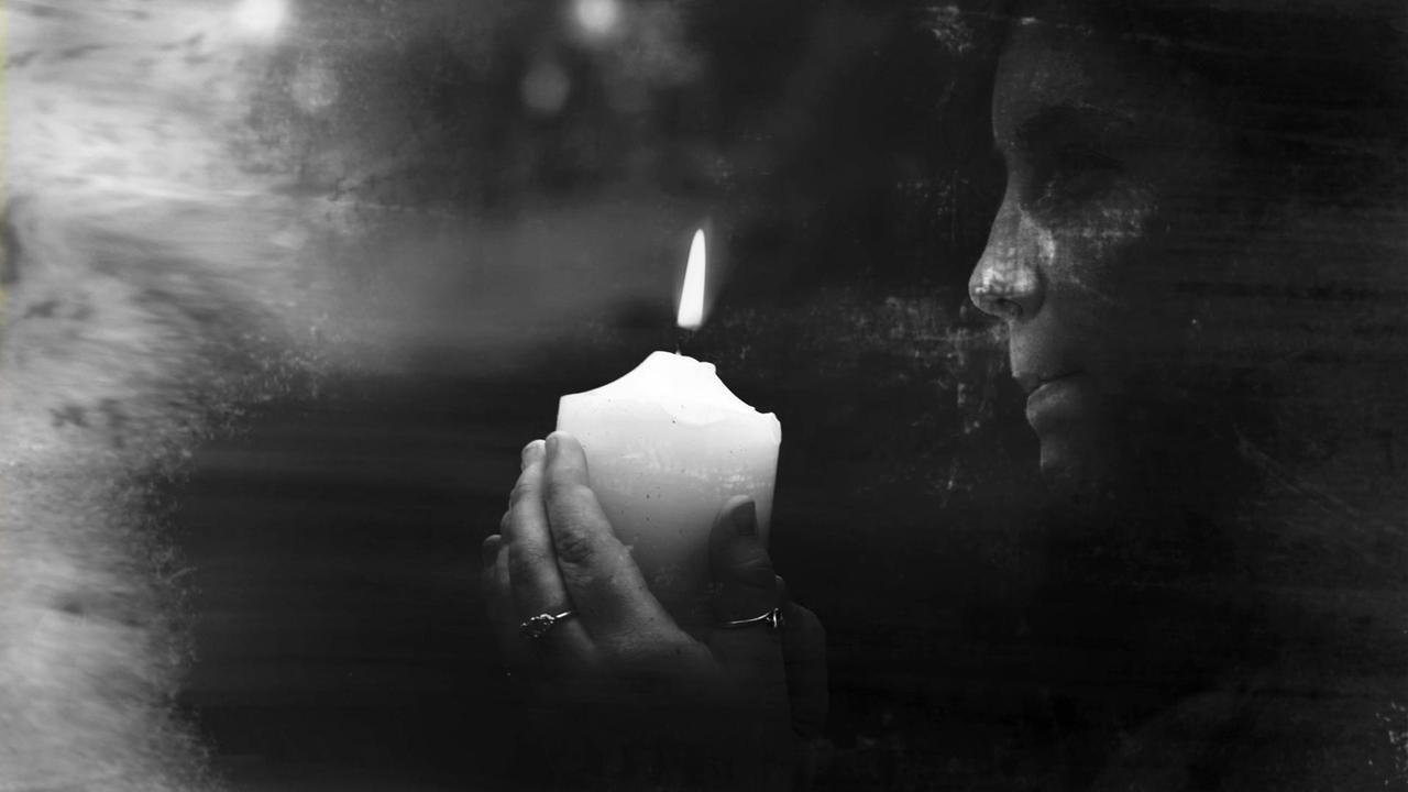 Schwarzweißfotografie einer weiblichen Hellseherin, die eine brennende Kerze in der Dunkelheit hält. Schwarzweißfotografie einer weiblichen Hellseherin, die eine brennende Kerze in der Dunkelheit hält.