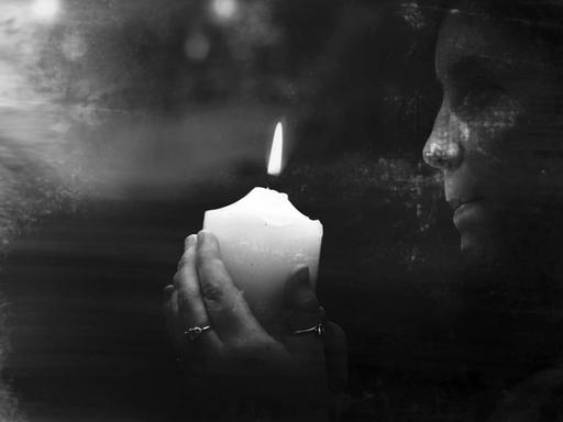Schwarzweißfotografie einer weiblichen Hellseherin, die eine brennende Kerze in der Dunkelheit hält.