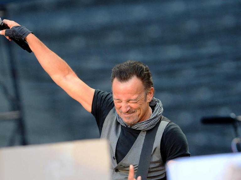 Der US-Rockstar Bruce Springsteen steht auf einer Bühne mit gesclossenen Augen und hält ein Mikrofon Richtung Publikum