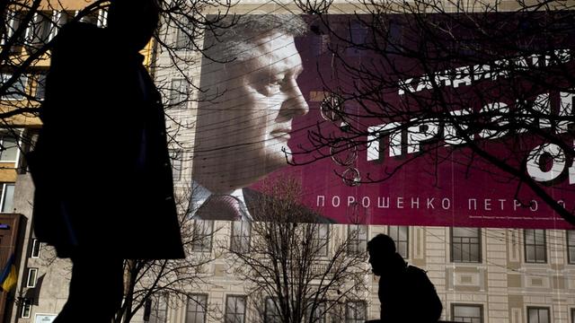 Fußgänger gehen an einem Plakat von Petro Poroschenko an einer Hauswand vorbei.