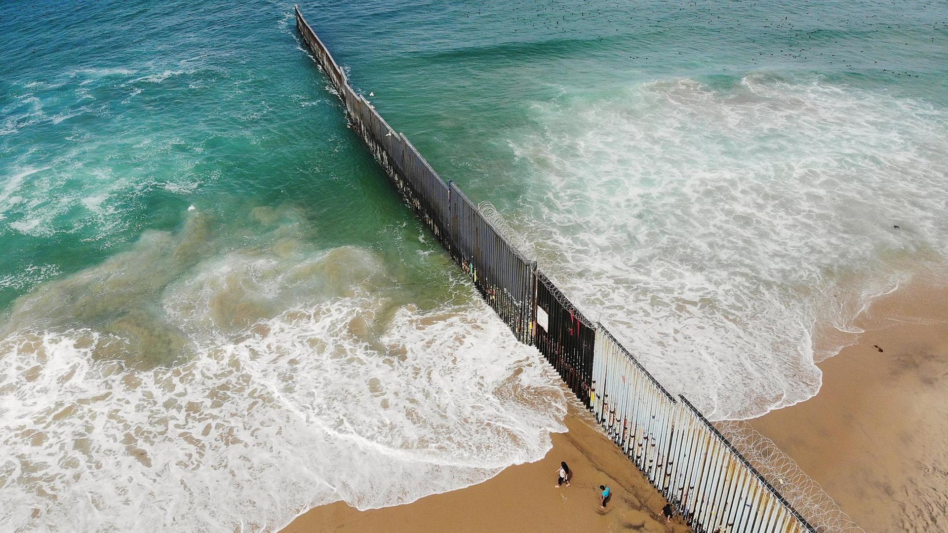 Eine Luftaufnahme zeigt Menschen, die auf der mexikanischen Seite der amerikanisch-mexikanischen Grenze am Strand von Tijuana am Grenzzaun stehen. Eine Luftaufnahme zeigt Menschen, die auf der mexikanischen Seite der amerikanisch-mexikanischen Grenze am Strand von Tijuana am Grenzzaun stehen.