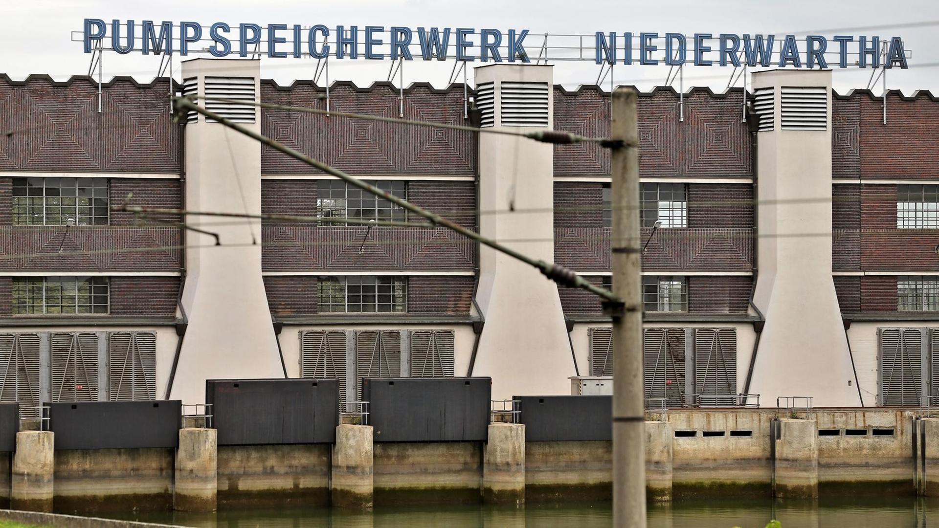 Industriebauten aus rotem Klinker, unterbrochen von weißen Kaminen. Darüber der blaue Schriftzug "Pumpspeicherwerk Niederwartha".