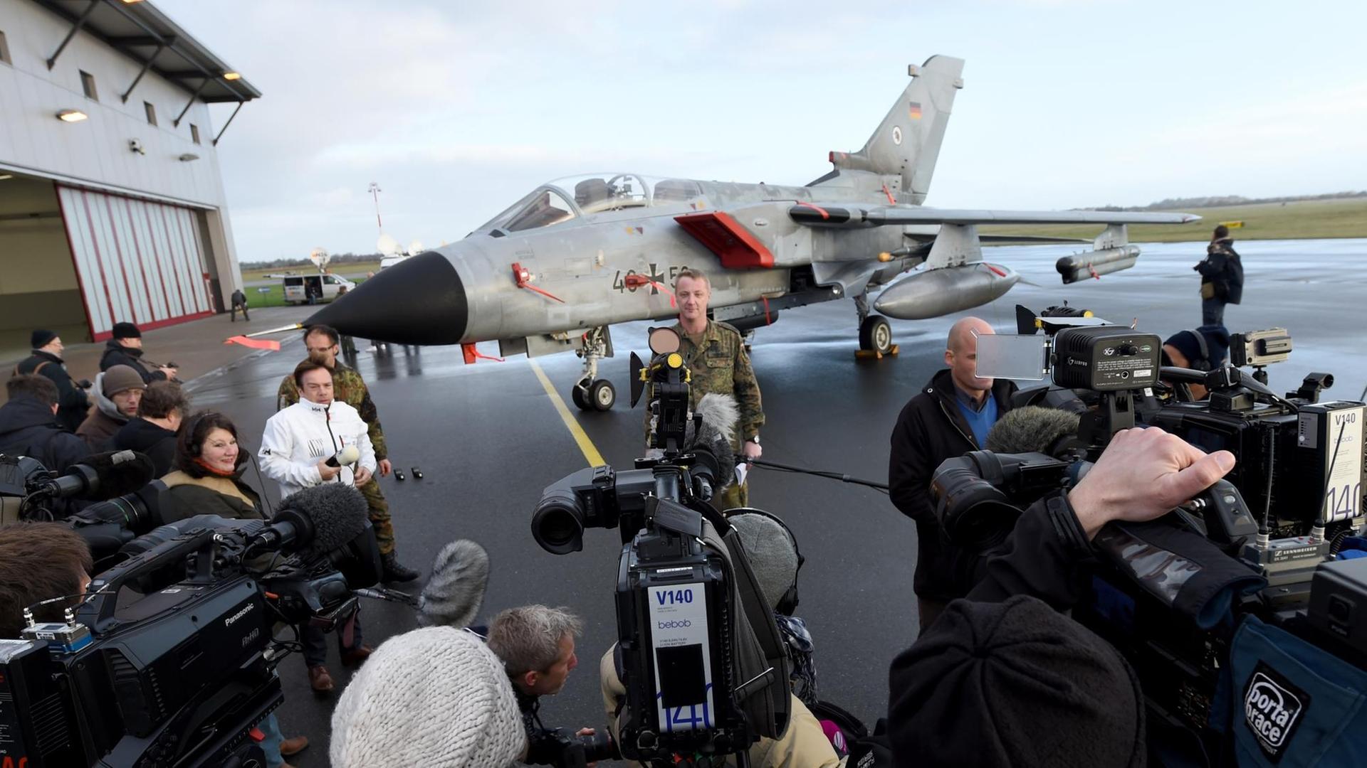 Zu sehen ist im Hintergrund ein Tornado-Kampfjet, davor stehen Journalisten mit Kameras und ein Bundeswehr-Soldat. Zu sehen ist im Hintergrund ein Tornado-Kampfjet, davor stehen Journalisten mit Kameras und ein Bundeswehr-Soldat.