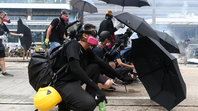 Das Bild zeigt protestierende Menschen auf der Straße in Hongkong. Sie haben aufgespannte Regenschirme, um sich vor der Polizei zu schützen.