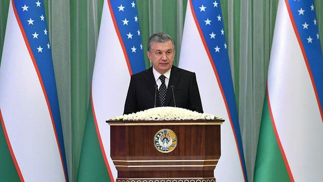 Shavkat Mirziyoyev steht an einem Rednerpult, im Hintergrund mehrere Landesflaggen.