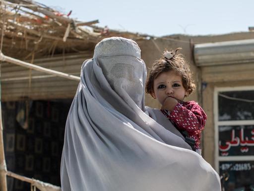 Am Stadtrand von Kandahar ist eine verhüllte Bettlerin mit ihrem Kind zu sehen, die auf Spenden aus den vorbeifahrenden Autos hofft.