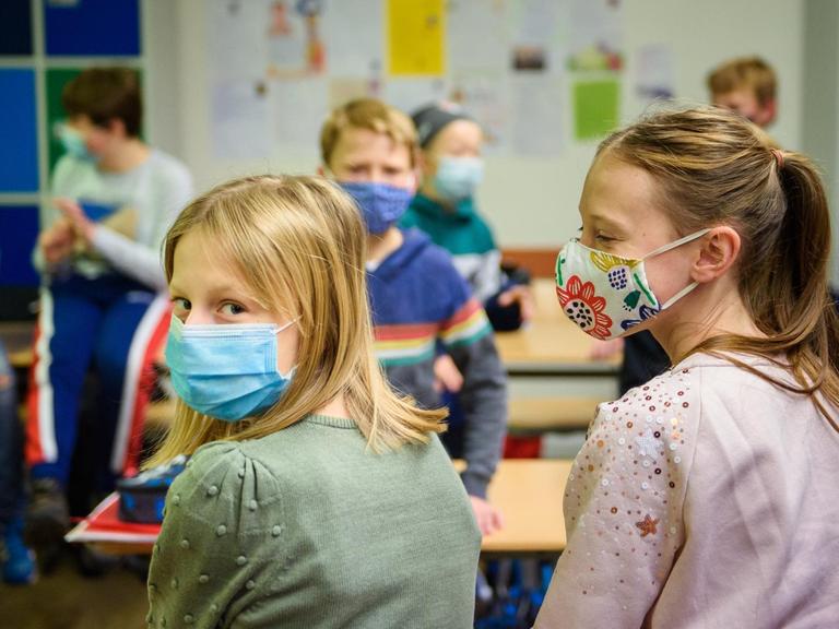 Schülerinnen und Schüler sitzen in einem Klassenzimmer und tragen dabei einen Mund-Nasen-Schutz.