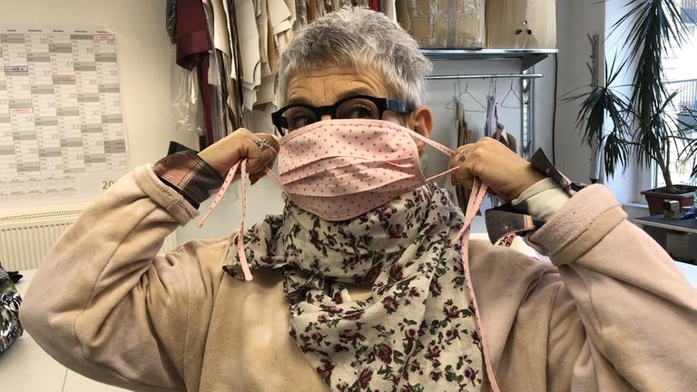 Susanne Zmudzinski mit einem selbstgenähten Mundschutz. Eine Frau mit kurzen grauen Haaren bindet sich einen pinken Mundschutz um. Susanne Zmudzinski mit einem selbstgenähten Mundschutz. Eine Frau mit kurzen grauen Haaren bindet sich einen pinken Mundschutz um.
