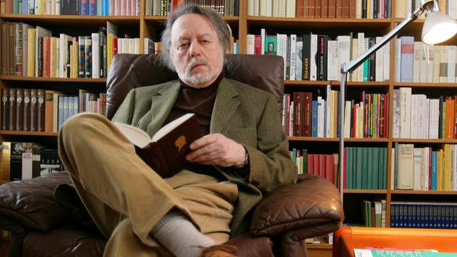 Der Schriftsteller Ror Wolf sitzt am Dienstag (26.02.2008) in seiner Wohnung in Mainz vor einem Bücherregal und blättert in einem Buch.