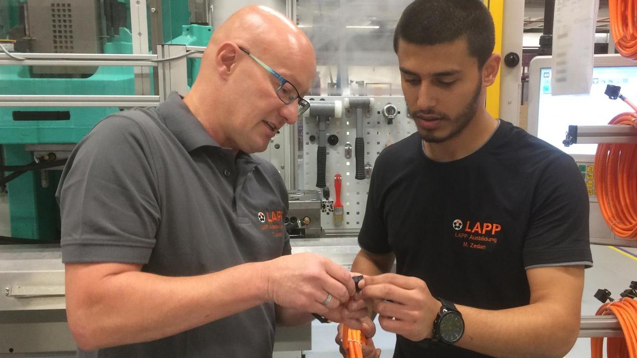 Thilo Linder zeigt einem Auszubildenden in einer Fabrik ein Detail Thilo Linder zeigt einem Auszubildenden in einer Fabrik ein Detail