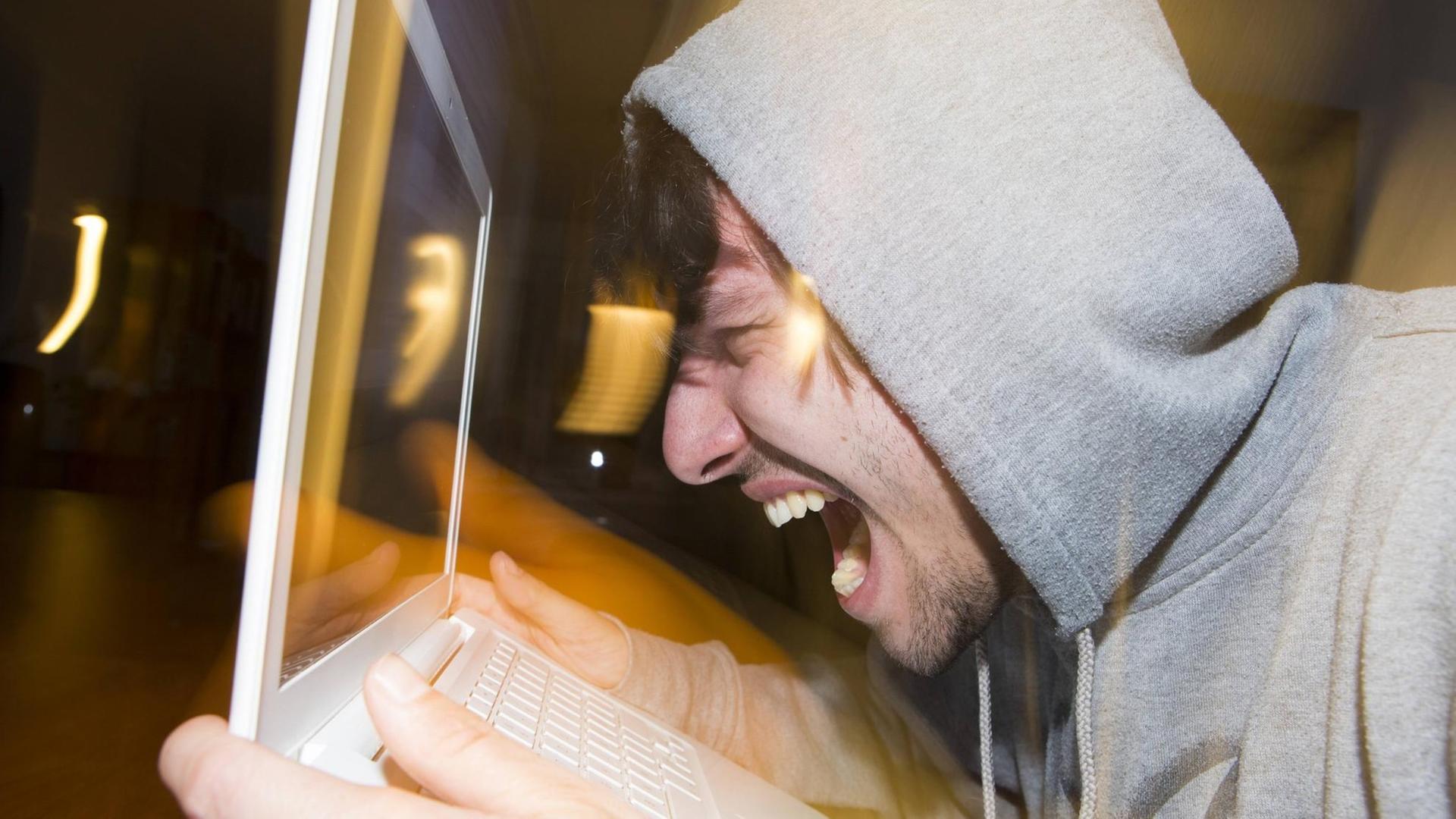 Ein junger Mann schreit seinen Laptop an Ein junger Mann schreit seinen Laptop an