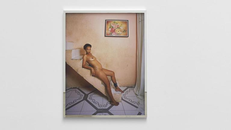 Das Foto zeigt eine ausgestellte Fotografie in der Kunsthalle Basel. Das Foto von Deana Lawson bildet eine junge Afroamerikanerin in nackter Pose und mit elektronischer Fußfessel ab.