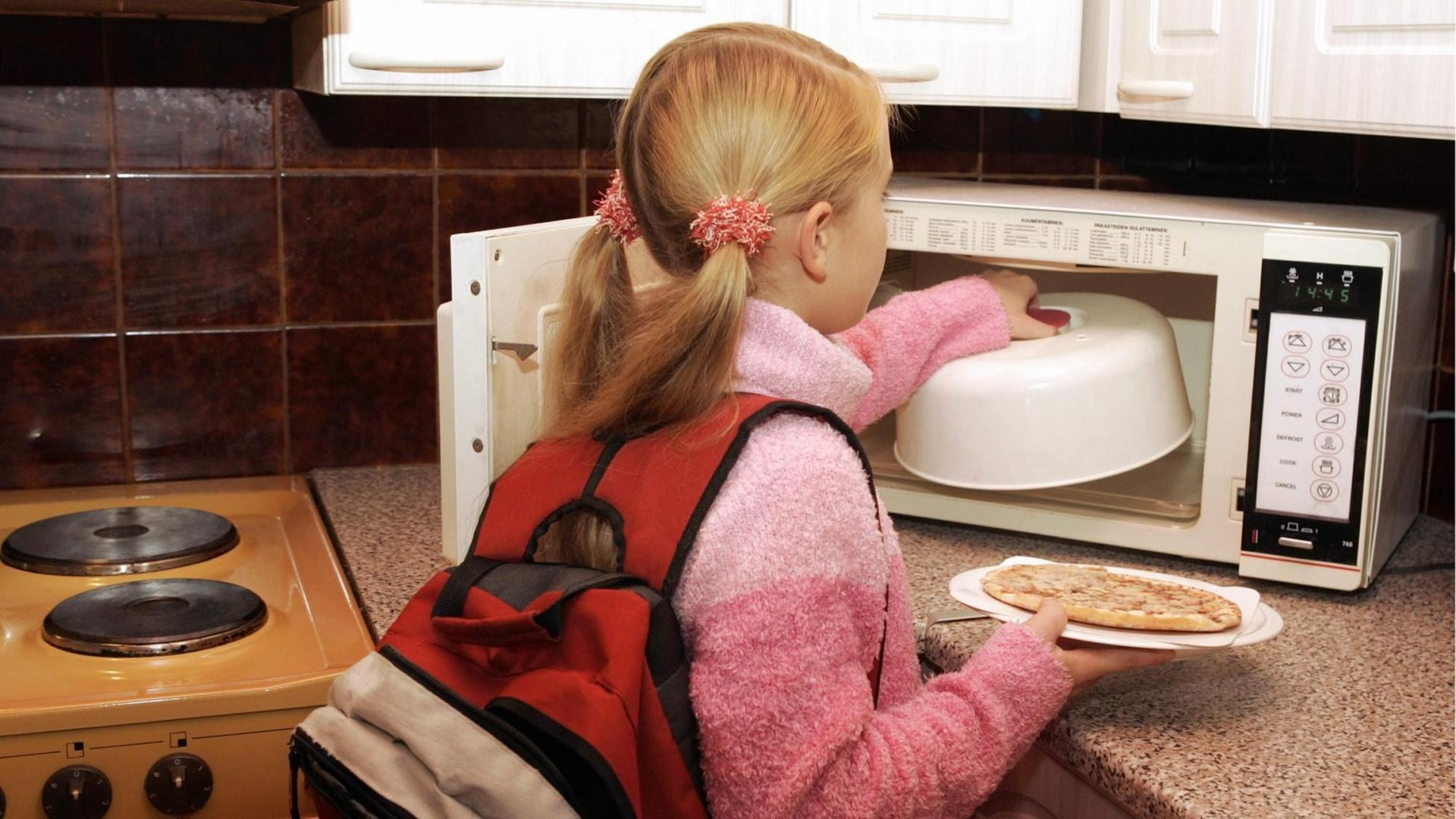 Ein junges Mädchen, das gerade von der Schule nach Haus gekommen ist, wärmt sich in der Mikrowelle etwas zu Essen auf. Ein junges Mädchen, das gerade von der Schule nach Haus gekommen ist, wärmt sich in der Mikrowelle etwas zu Essen auf.