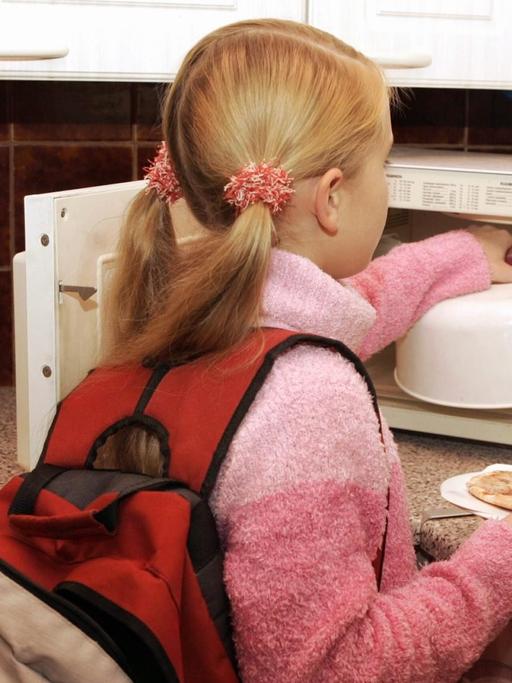 Ein junges Mädchen, das gerade von der Schule nach Haus gekommen ist, wärmt sich in der Mikrowelle etwas zu Essen auf.