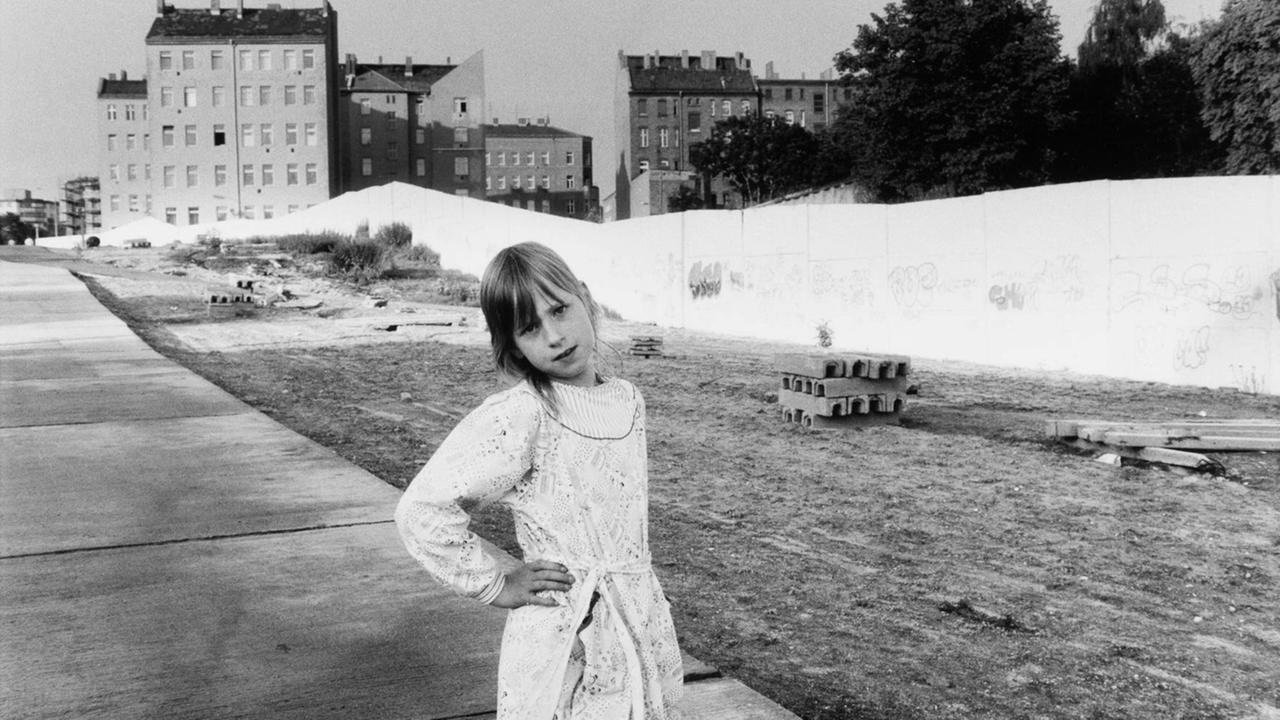 Fotografie von Sibylle Bergemann. Das Schwarzweiß-Foto zeigt ein kleines Mädchen in der Berliner Bernauer Straße. Im Hintergrund ist die Berliner Mauer zu sehen.