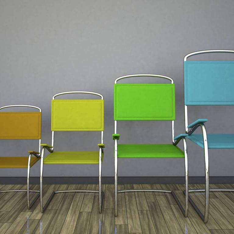 Fünf  Stühle in verschiedenen Farben und Größen stehen nebeneinander. Von links nach rechts werden die Stühle immer größer.