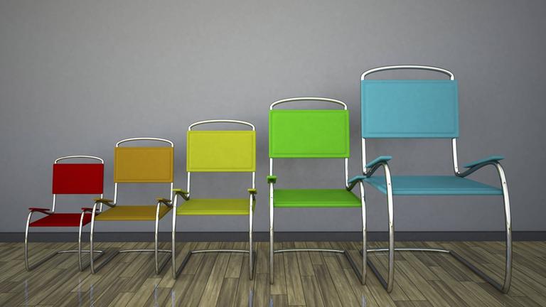 Fünf  Stühle in verschiedenen Farben und Größen stehen nebeneinander. Von links nach rechts werden die Stühle immer größer.