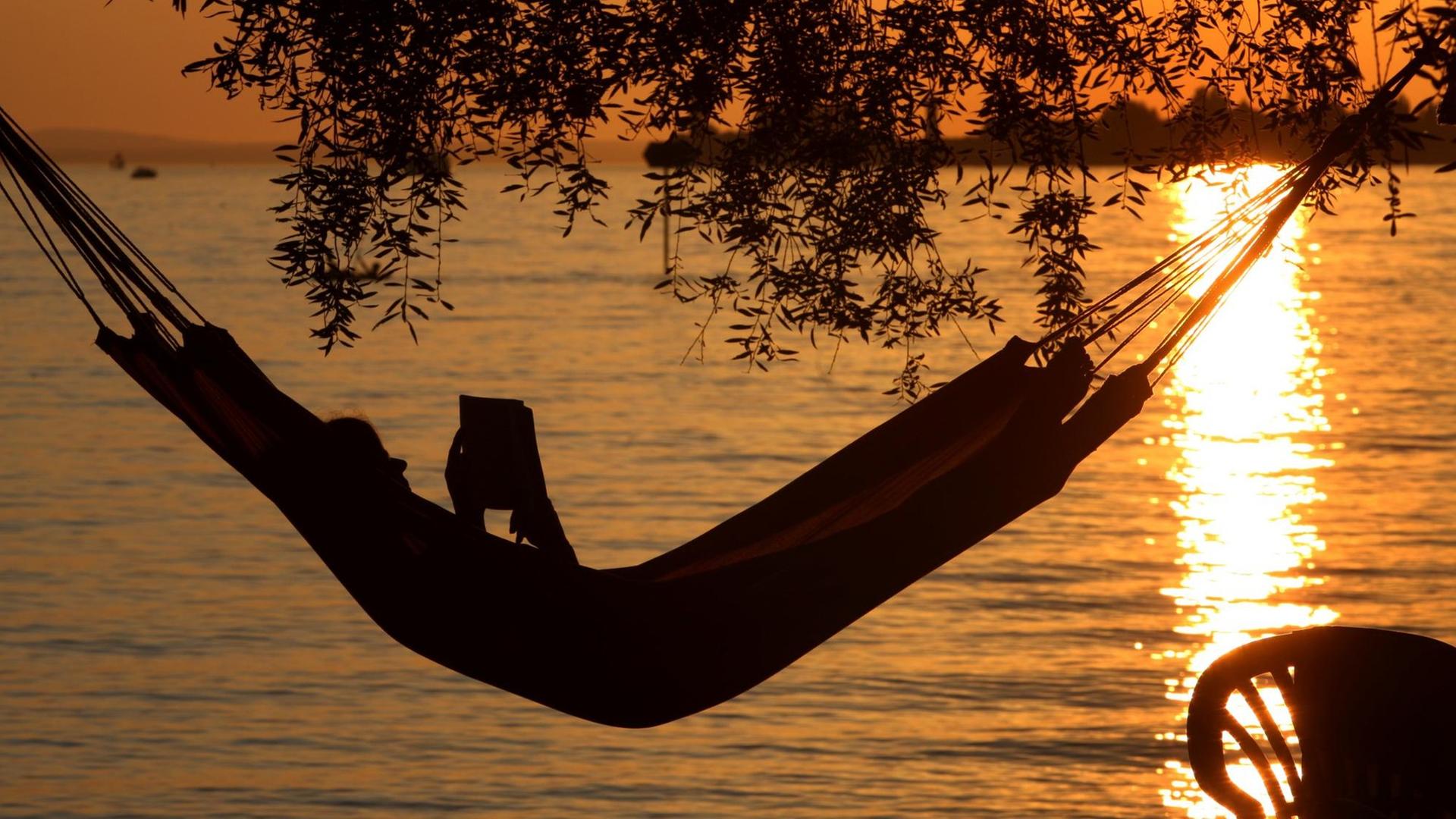 Eine Frau liest in einer Hängematte am Badestrand eines Campingplatzes in Lindau ein Buch. Eine Frau liest in einer Hängematte am Badestrand eines Campingplatzes in Lindau ein Buch.