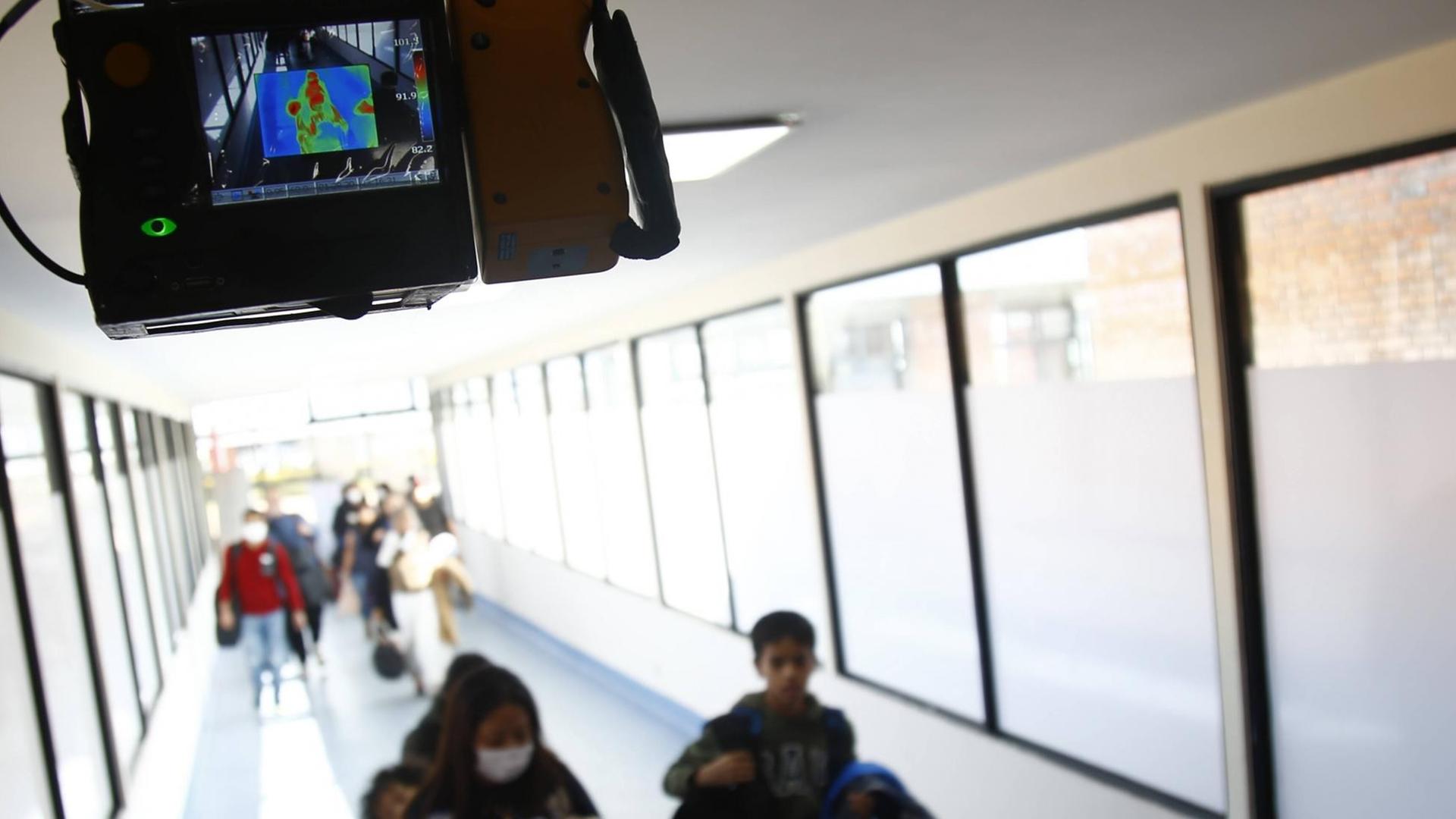 Ankommende Fluggäste im nepalesischen Kathmandu auf einem Laufband, oben auf einem Monitor ein Infrarotbild derselben Szene Ankommende Fluggäste im nepalesischen Kathmandu auf einem Laufband, oben auf einem Monitor ein Infrarotbild derselben Szene
