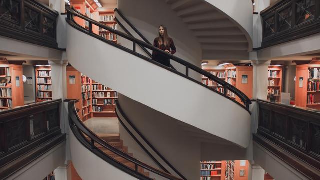 Eine junge Frau steht auf einer Treppe in einer Bibliothek.