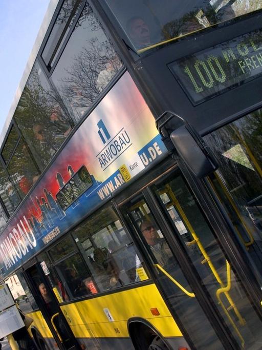 Auf dem Foto ist ein gelber Doppeldecker-Bus der Linie 100 zu sehen. Er verbindet den Westen mit dem Osten Berlins. Im Hintergrund ist die Siegessäule zu sehen.