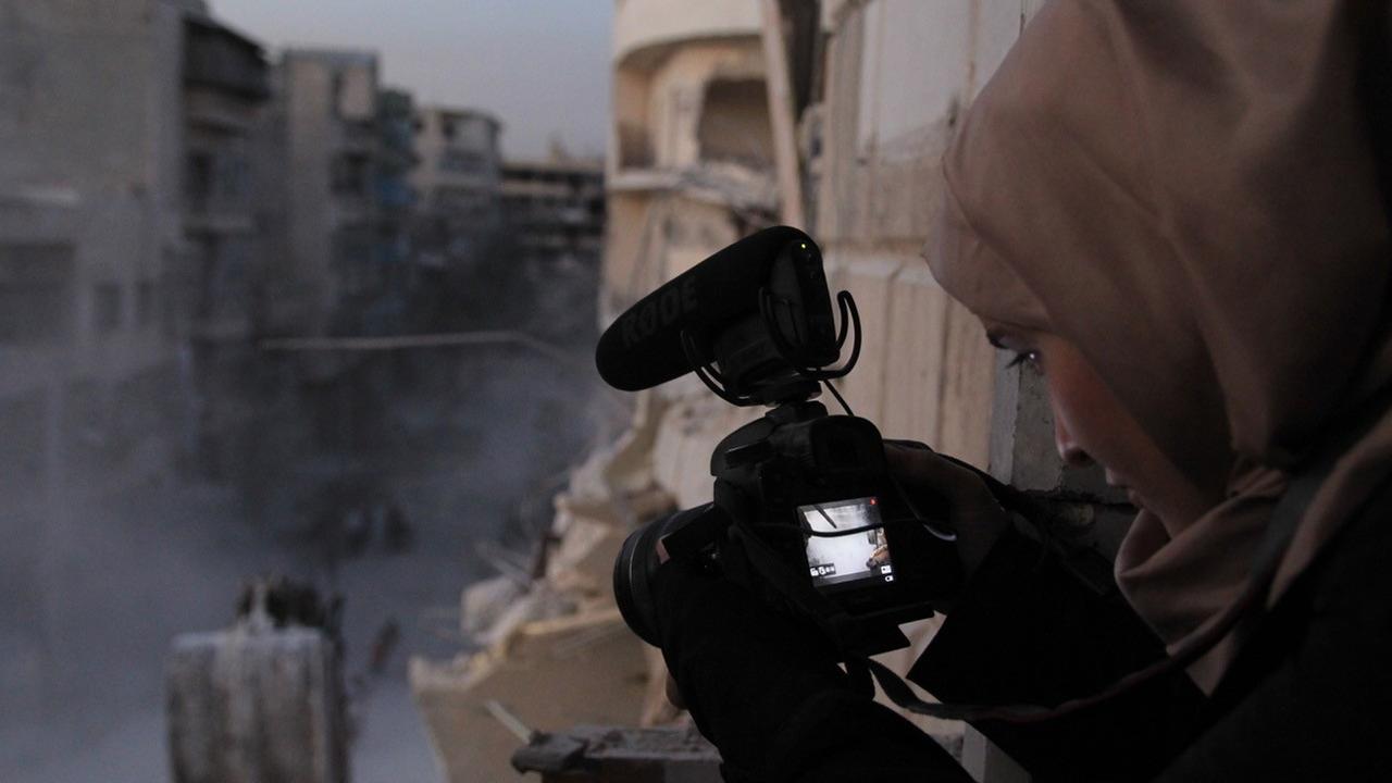 Filmszene aus "For Sama" aus der Reihe "Spotlight" beim Arabischen Filmfestival. Eine junge Frau mit Kopftuch filmt aus einem Fenster eine zerstörte Straße. Filmszene aus "For Sama" aus der Reihe "Spotlight" beim Arabischen Filmfestival. Eine junge Frau mit Kopftuch filmt aus einem Fenster eine zerstörte Straße.