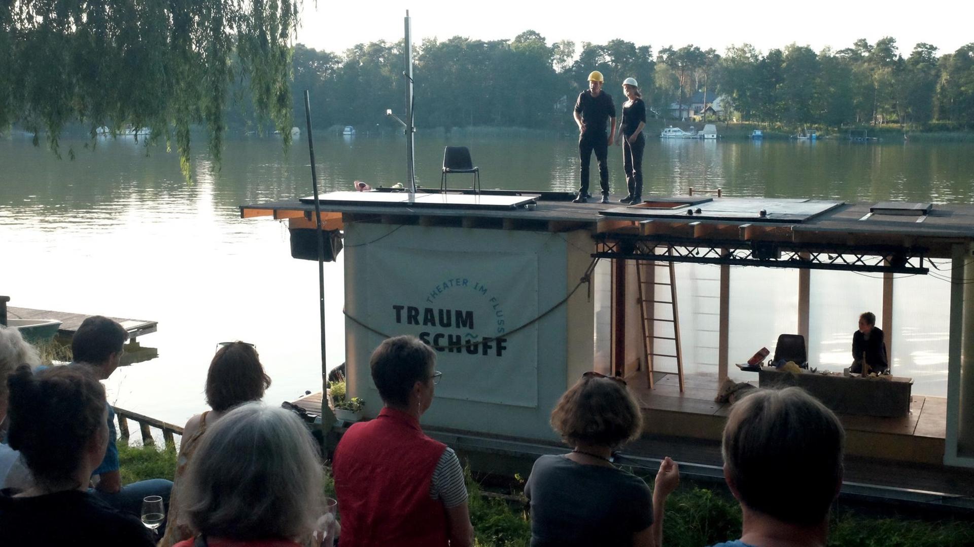 Das Traumschüff ankert am Flussufer, am Ufer sitzt Publikum und sieht die Vorstellung, die auf dem Oberdeck stattfindet. Das Traumschüff ankert am Flussufer, am Ufer sitzt Publikum und sieht die Vorstellung, die auf dem Oberdeck stattfindet.