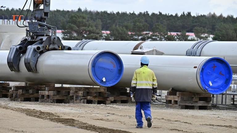 In Lubmin in Mecklenburg-Vorpommern werden Röhren für die Gaspipeline Nord Stream 2 verlegt. Daneben steht ein Arbeiter.